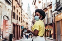 Portrait of black girl with face mask, afro hair and hoop earrings walking down a central street of the old city. — Stock Photo