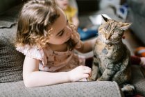 Little girl playing with her cat on the couch in the living room — Stock Photo