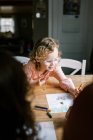 A toddler girl with glasses coloring with her family together at table — Stock Photo