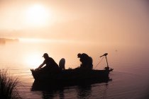 Silhouette Bootsfahrer auf idyllischem See bei buntem nebligem Sonnenaufgang — Stockfoto