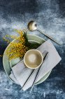 Ajuste de mesa con flores de mimosa amarillo brillante y vajilla gris sobre fondo de hormigón - foto de stock