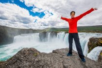 Uomo in piedi sulla cascata con uno zaino e una bandiera di iceland — Foto stock