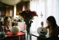 Две сестры рисуют тыквы на Хэллоуин за кухонным столом — стоковое фото
