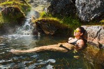 Giovane donna in costume da bagno con cascata in montagna — Foto stock