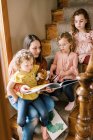 A young mother and her three girls sitting on stair case reading books — Stock Photo