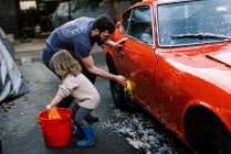 Bambina che pulisce una macchina classica rossa con suo padre insieme — Foto stock