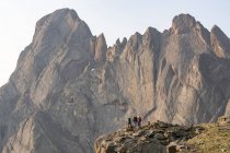 Mochileros masculinos y femeninos de pie contra acantilado rocoso mientras mochileros durante las vacaciones - foto de stock
