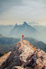 Wanderer mit rotem Hemd steht auf Berggipfel mit malerischer Aussicht dahinter — Stockfoto