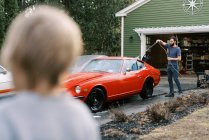 Маленькие дети помогают отцу помыть классическую красную машину снаружи. — стоковое фото