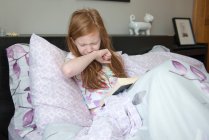 Malade petite fille lecture dans le lit — Photo de stock