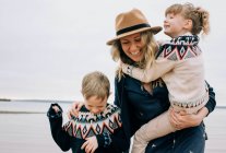 Mamá y sus hijos abrazándose y riendo en la playa en un día nublado - foto de stock