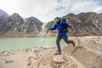 Backpacker hikes over boulders next to glacial fed lake. — Stock Photo