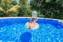 Mulher jovem na piscina segurando bola de praia — Fotografia de Stock