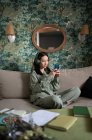 Asiatico femminile ascolto di musica e navigazione cellulare mentre si riposa sul divano — Foto stock