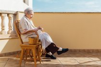 Ältere Frau näht mit Nadel und Faden auf Außenterrasse — Stockfoto
