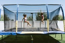Irmãs desfrutando de verão no trampolim com um aspersor — Fotografia de Stock