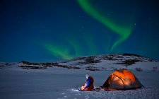 Cientista senta-se fora de sua tenda com luzes do norte no céu — Fotografia de Stock