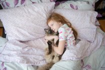 Krankes kleines Mädchen kuschelt Katze im Bett — Stockfoto