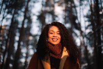 Porträt einer lächelnden jungen Frau, die im Winter zwischen Bäumen steht — Stockfoto
