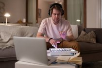 Мужчина ди-джей в наушниках, слушающий музыку и пользующийся звуковой доской на диване дома — стоковое фото