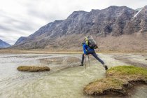 Backpacker utilizza bastoncini da trekking per saltare attraverso un profondo canale fluviale — Foto stock