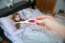 Mão segurando termômetro, menina na cama doente — Fotografia de Stock