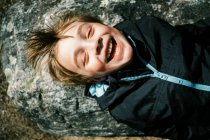 Niño acostado en la roca y disfrutando de los primeros rayos de sol cálidos en la cara - foto de stock