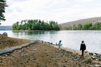 Two kids playing at the rocky beach of a lake surrounded by forest — Stock Photo
