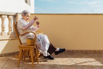 Donna anziana che cuce con ago e filo sulla terrazza esterna — Foto stock