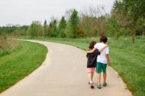 Un niño y una niña caminan brazo en brazo por sendero curvo en un parque - foto de stock