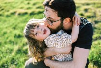 Feliz niña pequeña abrazando a su padre con gafas y sonriendo - foto de stock