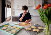 Молодий хлопчик прикрашає пасхальне печиво на стійці сучасної кухні . — стокове фото