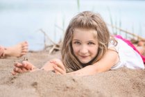 Bambina sdraiata nella sabbia vicino a un lago — Foto stock