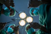 Equipe de cirurgiões com bisturi são operação em conjunto no fundo da lâmpada cirúrgica, Ponto de vista tiro. — Fotografia de Stock