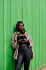 Черная женщина в городской одежде со смартфоном и музыкальными наушниками — стоковое фото