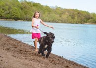 Bambina che corre su una spiaggia con cane nero — Foto stock