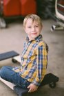 Little boy sitting on a hardwood dolly in his father's garage — Stock Photo