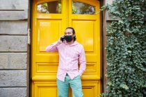 Молодий чоловік в масці для обличчя під час розмови по телефону на вулиці — стокове фото