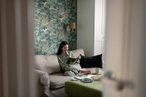 Mujer asiática relajándose en el sofá y leyendo libro en la elegante sala de estar en casa - foto de stock