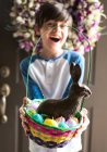 Jovem menino feliz segurando cesta de Páscoa cheia de ovos e coelho de chocolate — Fotografia de Stock