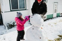 Father and daughter build snowman outside home — Stock Photo