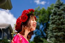 Una niña riendo con los ojos cerrados lleva una corona de rosas - foto de stock