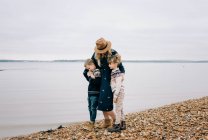 Mamma e i suoi figli camminano lungo la spiaggia abbracciandosi in una tranquilla giornata autunnale — Foto stock