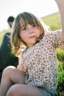 Kleines glückliches Mädchen sitzt lächelnd auf einem Hügel und berührt die Kamera — Stockfoto