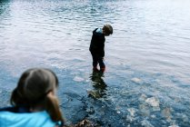 Menino em botas de borracha vermelha andando através de água azul intocada — Fotografia de Stock