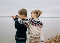 Brother and sister playing at the beach together pointing to the sea — Stock Photo