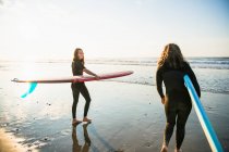 Дві жінки друзі збираються на схід сонця літній серфінг — стокове фото