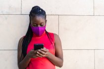 Mujer con trenzas africanas enviando un mensaje desde su teléfono inteligente - foto de stock