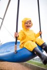 Felice bambino ragazzo cavalca su altalena al parco in una giornata umida — Foto stock