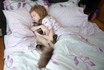 Enferma niña durmiendo en cama con gato - foto de stock